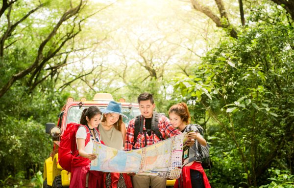 Hiking - hikers looking at map. Couple or friends navigating together smiling happy during camping travel hike outdoors in forest. Young mixed race Asian woman and man.